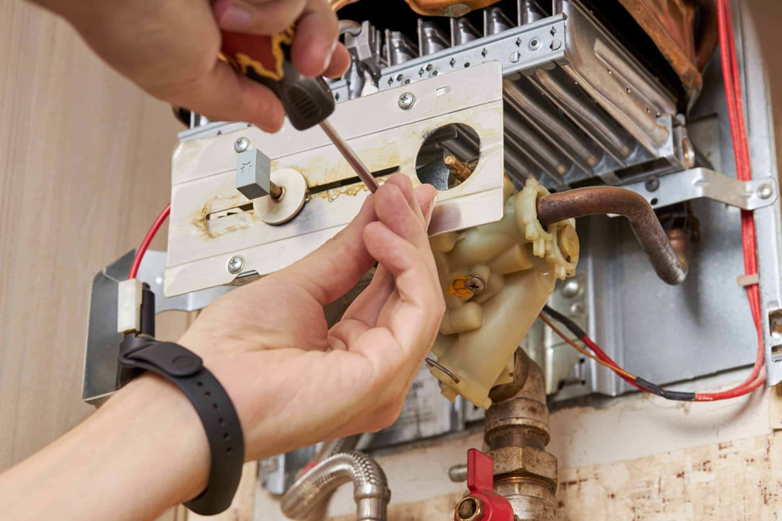 Close-up of hands using a screwdriver to repair or install parts in a heating or plumbing system. The image, showcasing intricate components and wiring within a metal casing, highlights the expertise of a skilled plumber in Plymouth County, MA.
