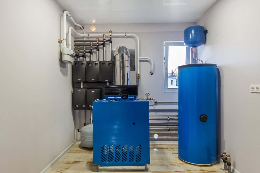 A modern boiler room with a blue heating system unit and a large blue water tank, surrounded by pipes and control panels, in a clean, well-lit space with white walls—a perfect setup for a skilled plumber Plymouth or Middlesex expert.