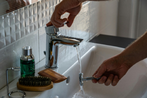 person rinsing a razor under running water from a faucet