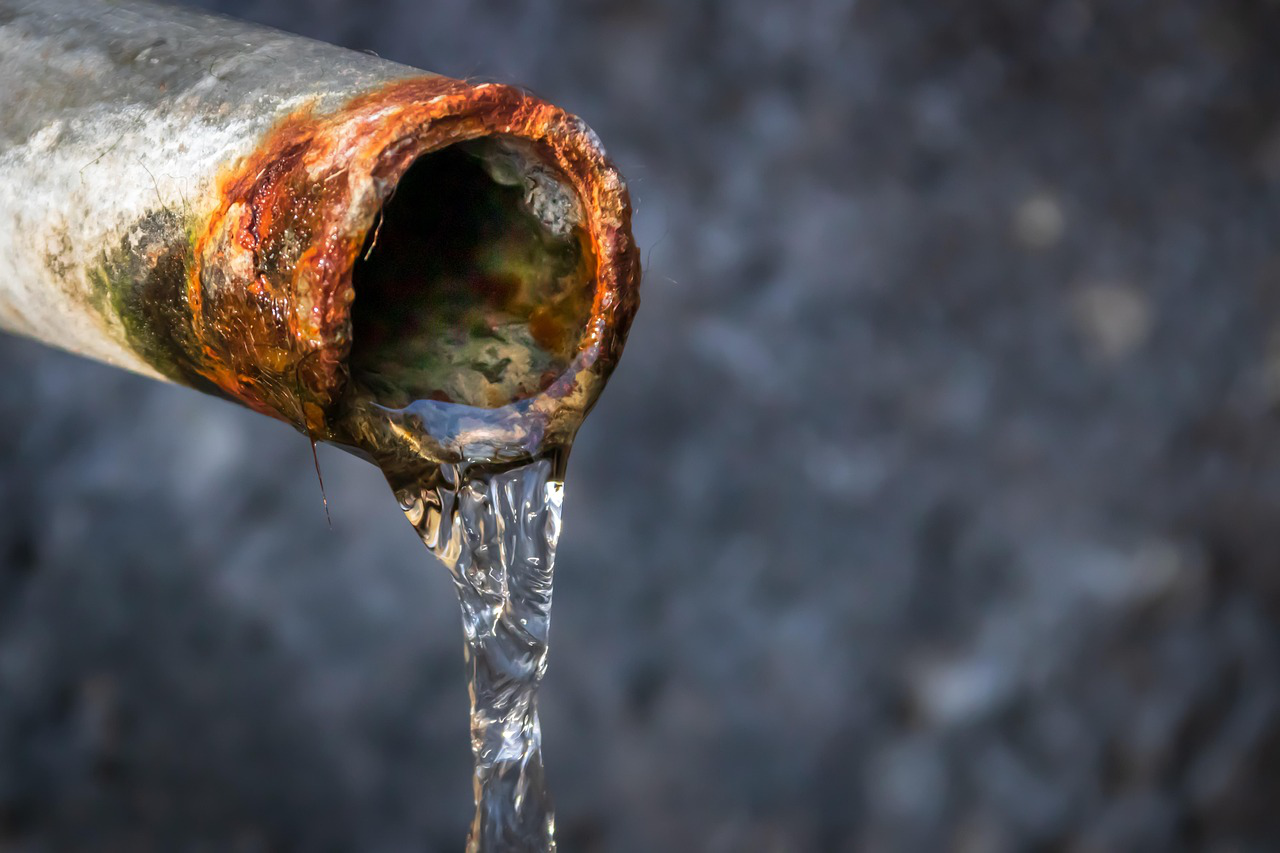 Close-up of a rusty, corroded metal pipe with water flowing out