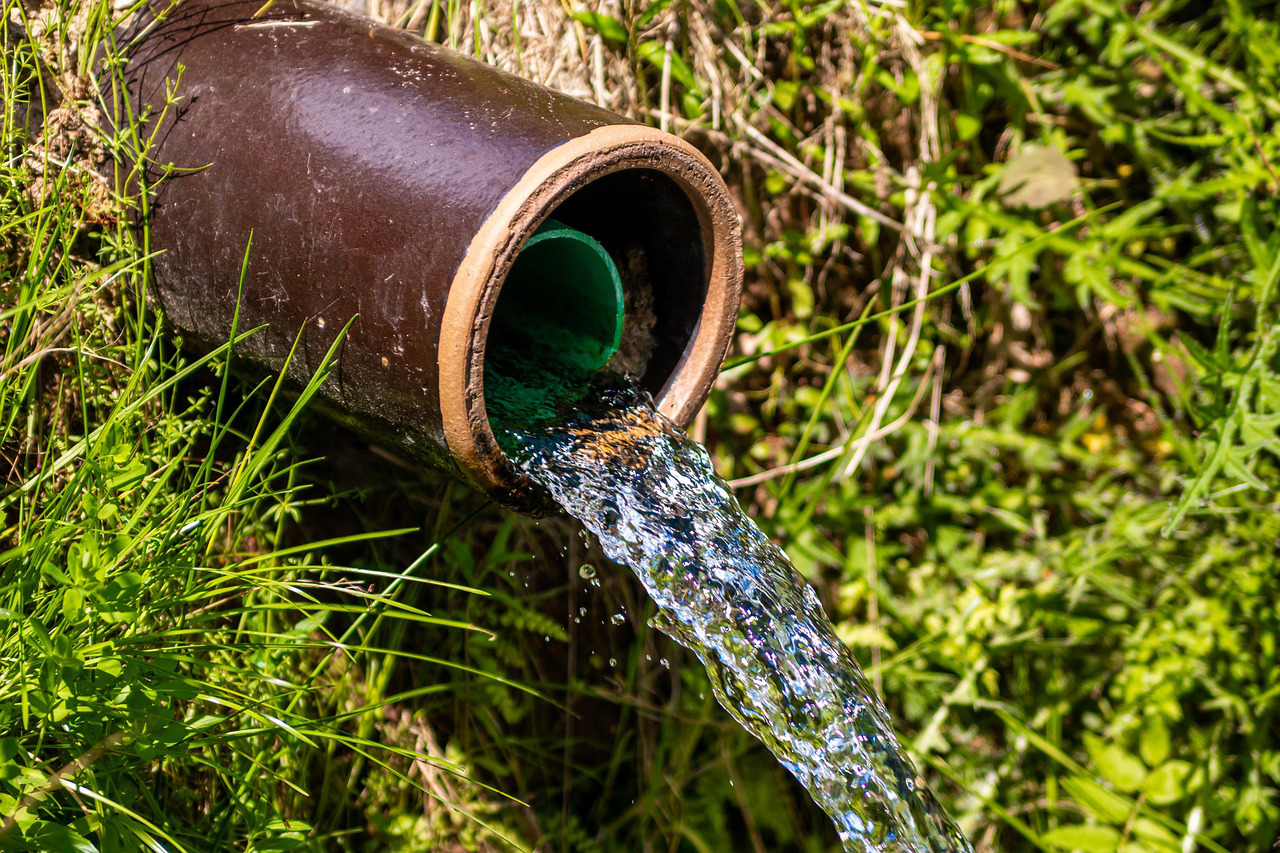 Water flowing out of a large outdoor drainage pipe surrounded by green grass