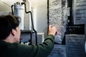A person points at instructions posted on a wall inside a room with various pipes and equipment nearby, highlighting notes about water use and film development—perhaps referencing guidance from a plumber Plymouth serving Middlesex and Suffolk County.