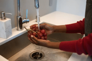A person washing grapes in a kitchen sink