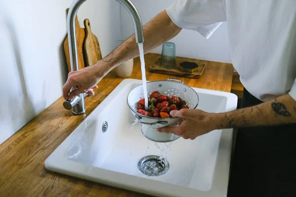 A person washing strawberries in a white kitchen sink