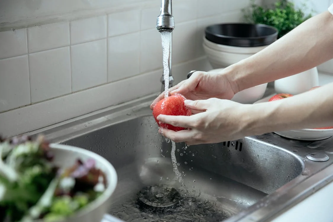  A person washing an apple using water from a faucet in a steel sink