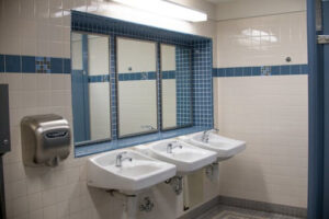 A clean public restroom in Middlesex features three white sinks, a large mirror above them, a stainless steel hand dryer on the wall, and blue and white tiled walls.