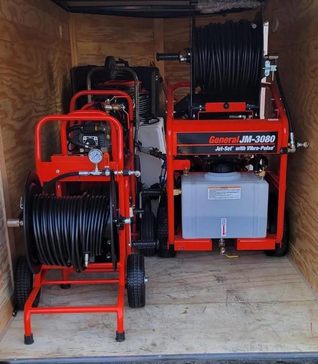 Two red industrial jetter machines labeled "General JM-3080 Jet-Set," with long black hoses, are set inside a wooden cargo trailer in Norfolk, MA. Other related equipment and tanks are also visible in the tight space.