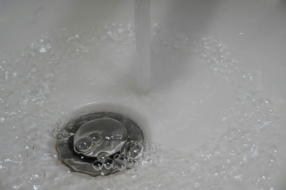 Water flows from a faucet into a sink in Bristol, creating bubbles and ripples as it drains around a metal sink stopper.