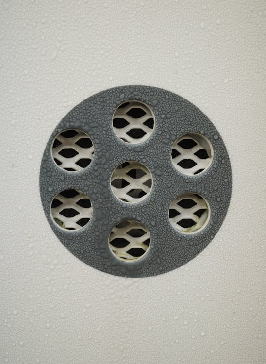 Close-up of a shower drain with water droplets, showing signs of water backing up that require expert plumbing help