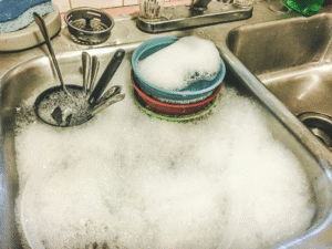 Kitchen sink filled with water and dirty dishes caused by a sewer line failure.
