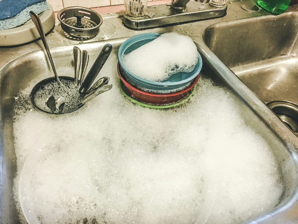 A kitchen sink filled with soapy water, foam, and a stack of colorful bowls—just another busy day in Middlesex. Several spoons and utensils are submerged in the soapy water, ready to be washed.